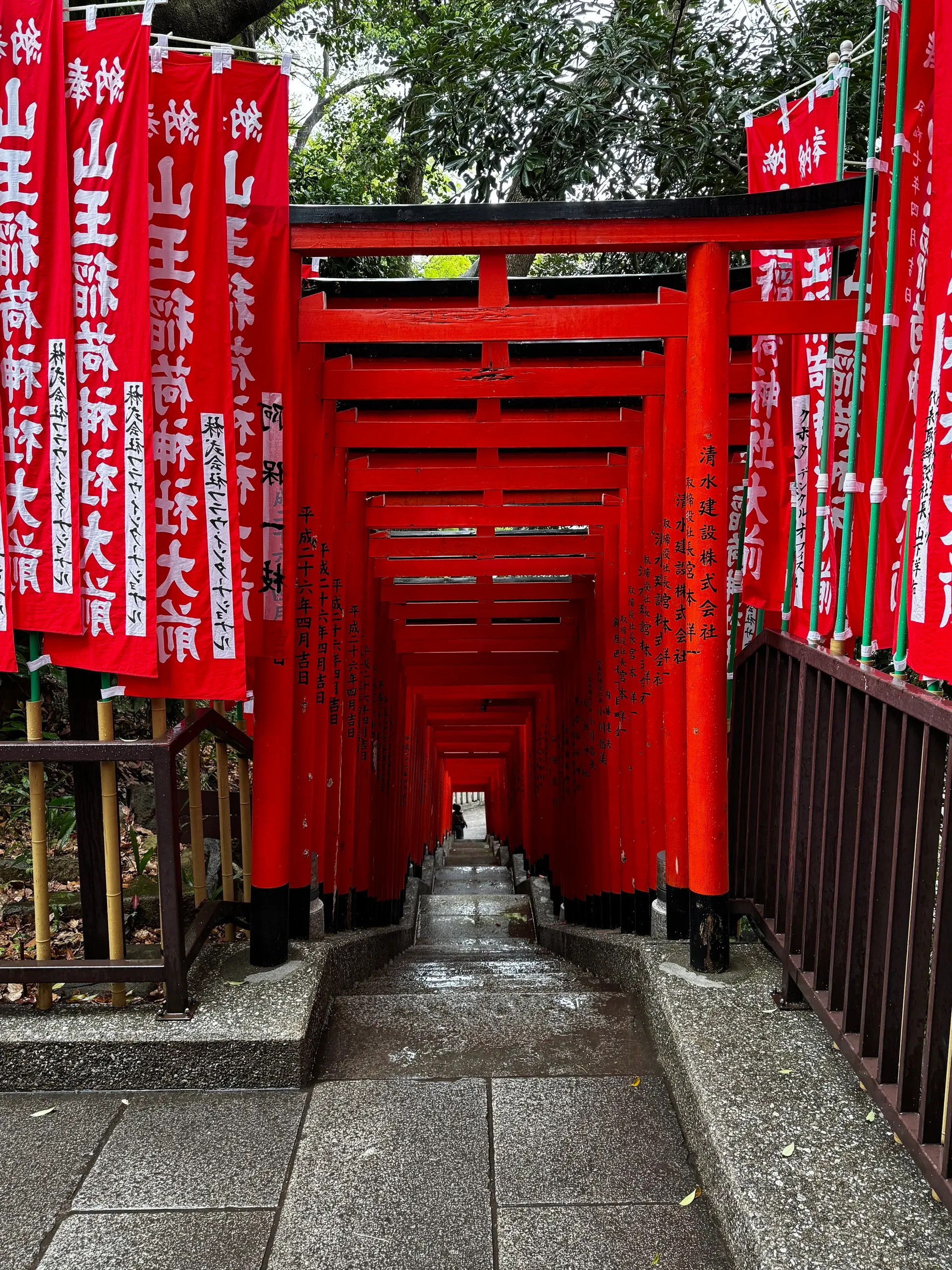 Allée de torii vermillon et de bannières rouges menant à un sanctuaire.
