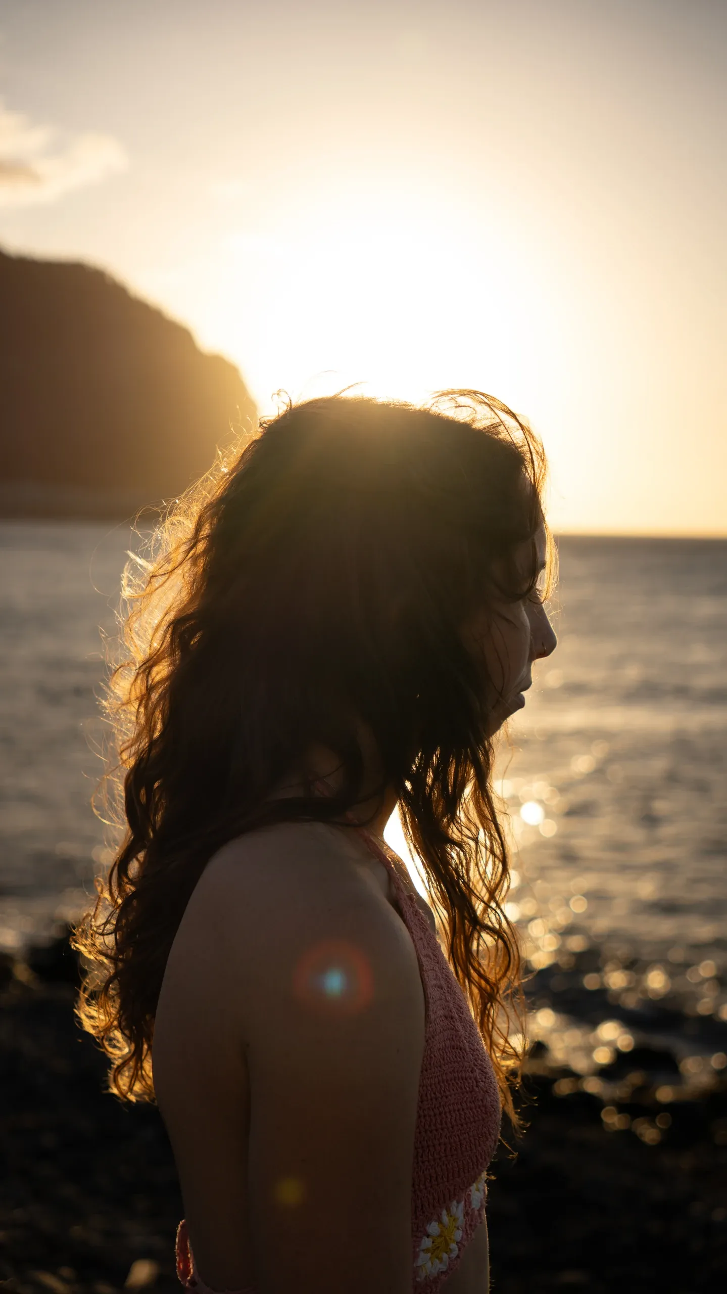 Camille à contre-jour face à la mer, au coucher du soleil.