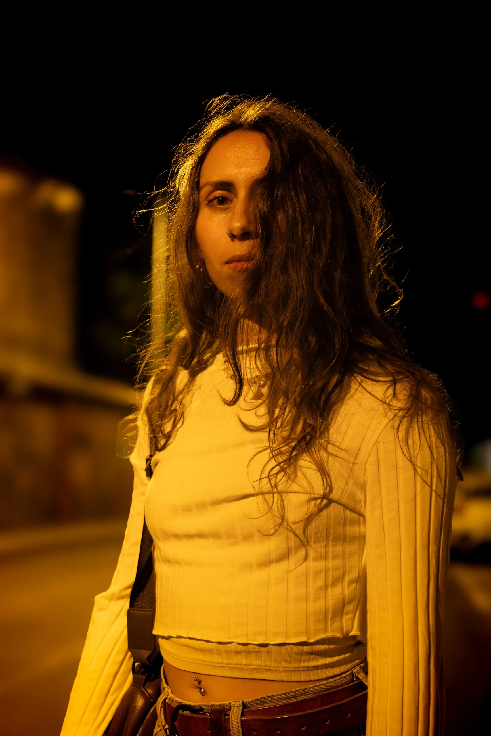 Portrait de nuit de Camille en haut jaune, éclairée par la lumière orangée de la rue.