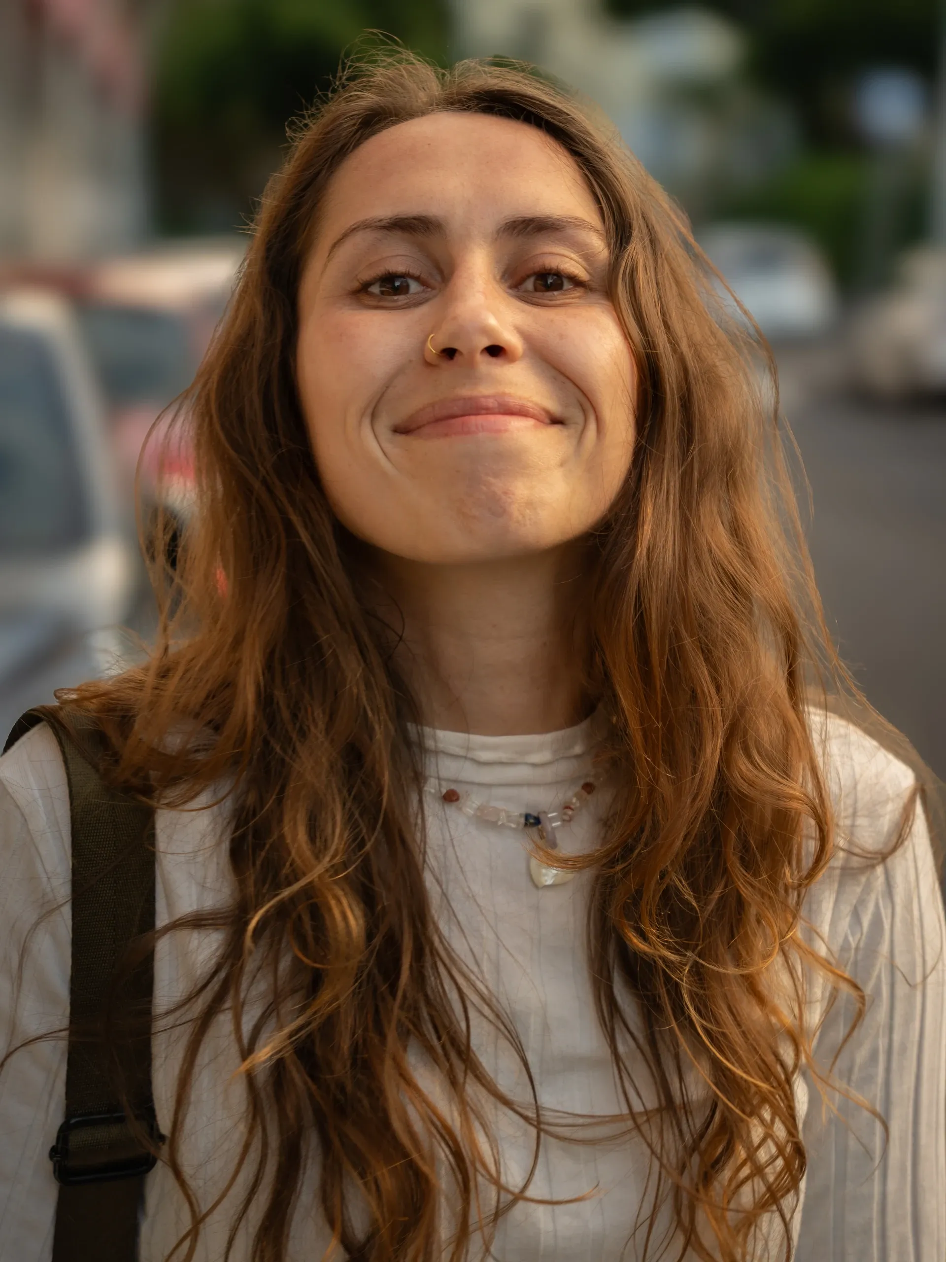 Portrait de Camille, longs cheveux bouclés, souriante dans une rue en journée.