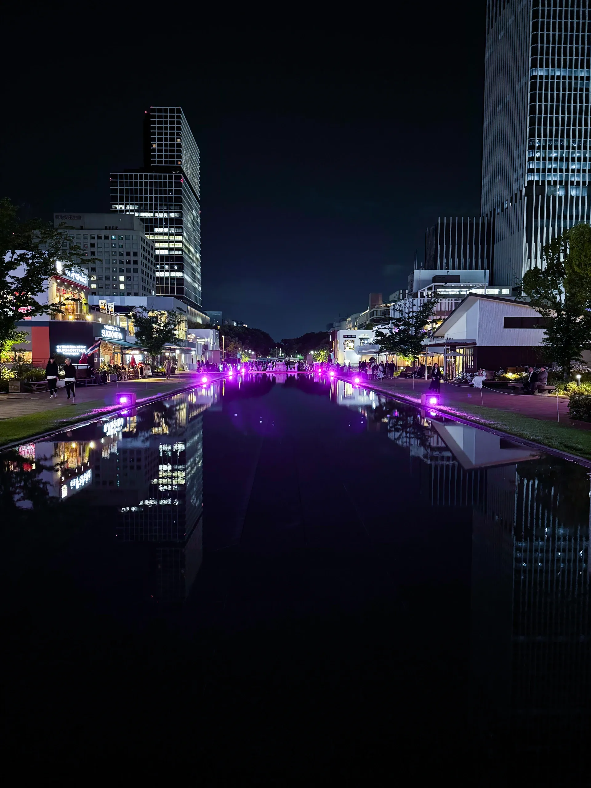 Canal en ville la nuit, reflets de néons violets entre les immeubles.