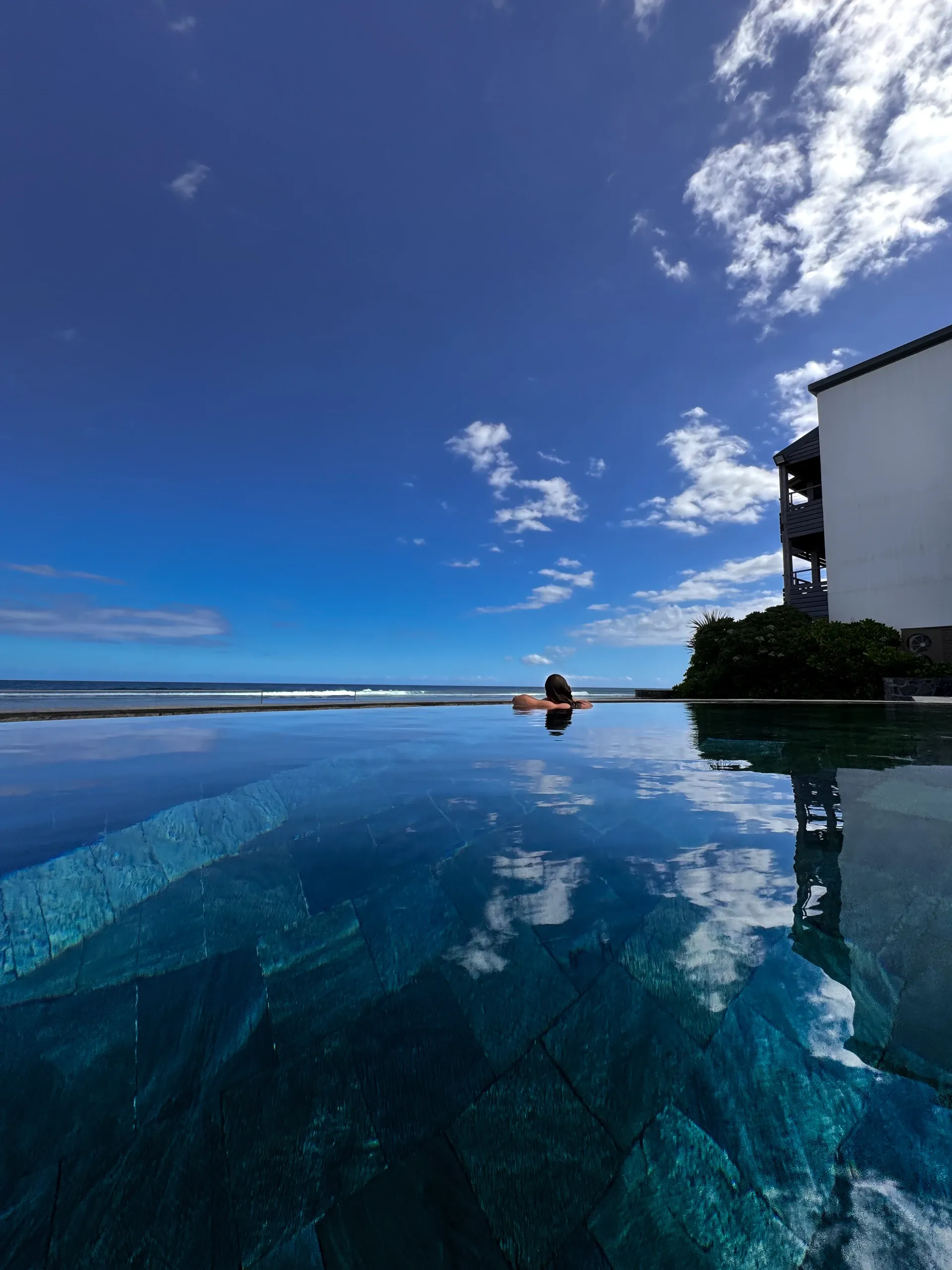 Piscine à débordement sous un ciel bleu, Dono au loin au bord de l'eau.