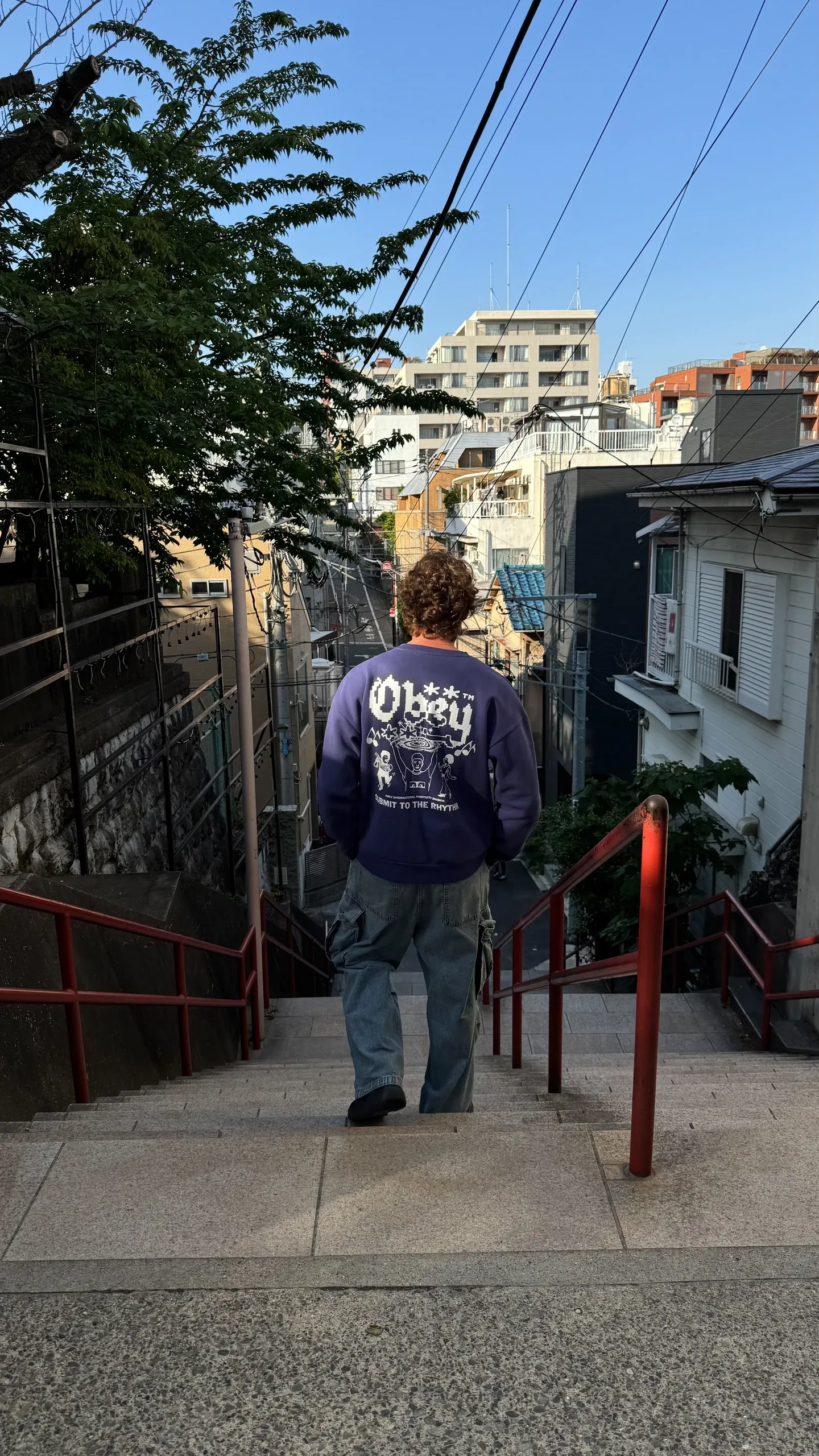 Dono de dos descend un escalier aux rampes rouges, dans une ruelle en pente entre les immeubles.