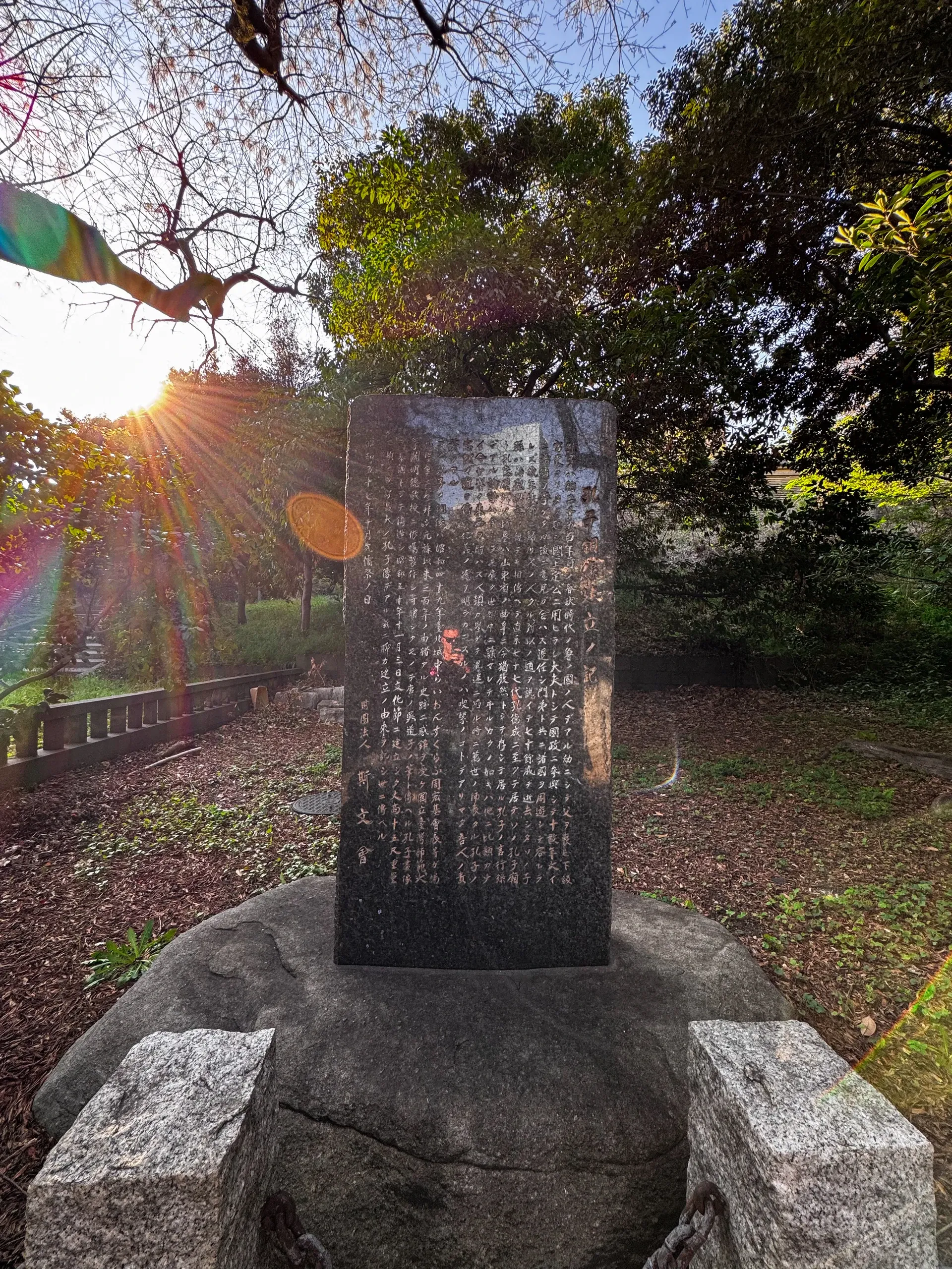Stèle de pierre gravée, le soleil perçant derrière les arbres.