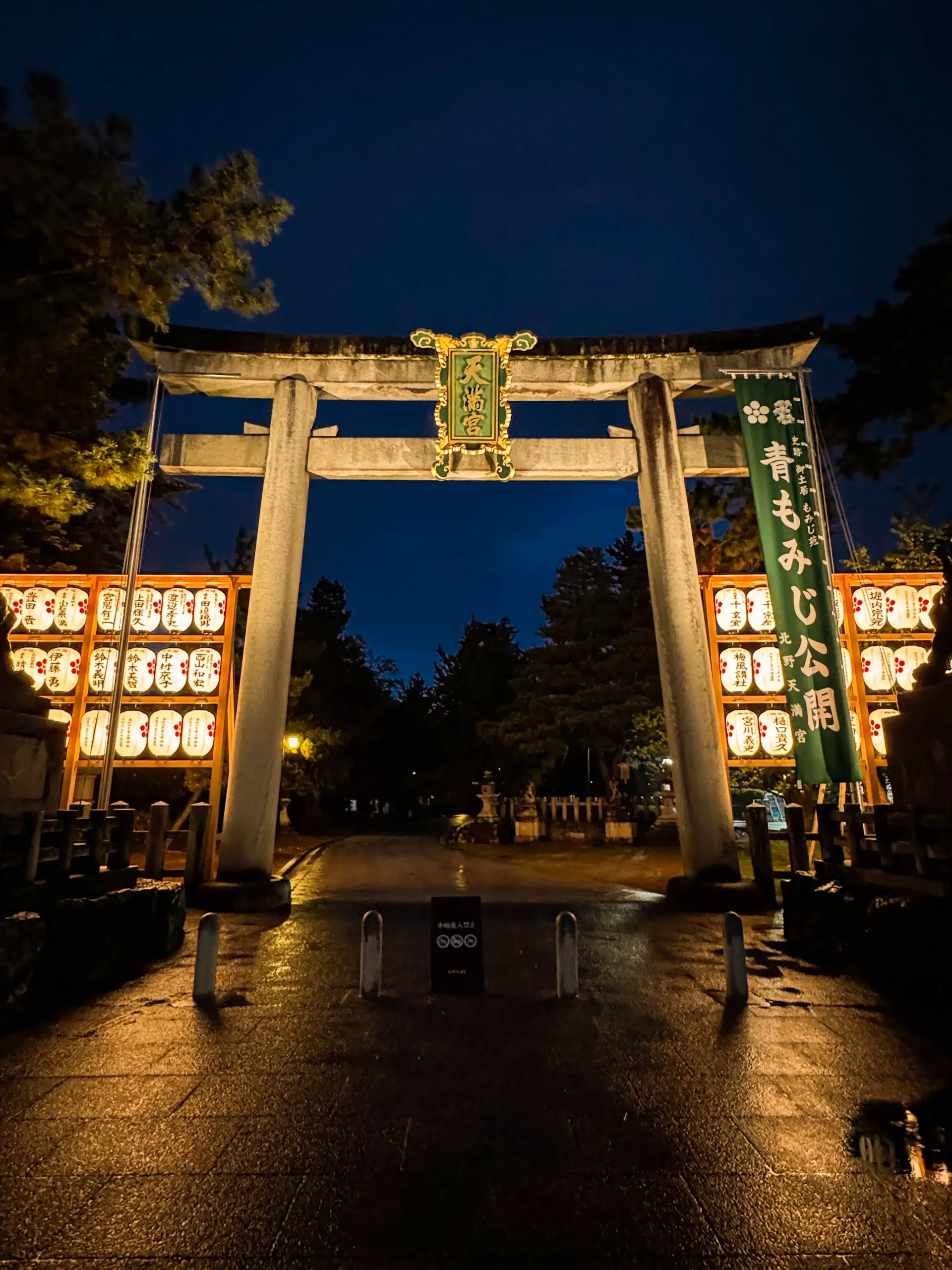 Torii de pierre éclairé de lanternes, la nuit, sous un ciel bleu profond.
